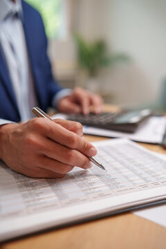 Business professional reviews financial records with a pen and calculator at a desk, representing audit, accounting, bookkeeping, financial analysis, reporting, accuracy and expense management.