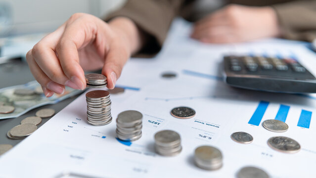 Businesswoman stacks coins on financial charts beside a calculator, representing saving, investment planning, budget management, financial growth, wealth building, income and future goals.