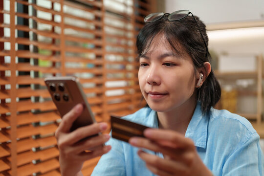 Asian Woman uses a smartphone while holding a credit card for mobile payment and online banking, representing secure digital transactions, e-commerce shopping