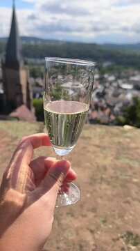 Vertical view of a champagne glass held in hand with a panoramic view of the historic city of Marburg, Germany, in the background. Elegant travel and celebration concept overlooking the city.