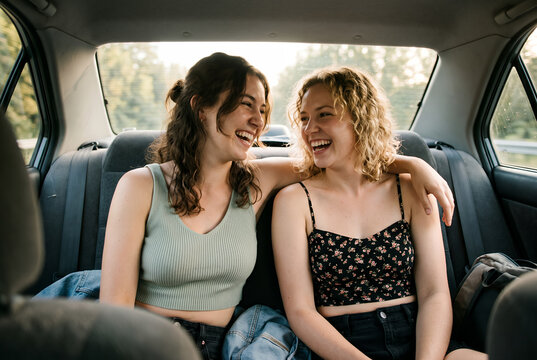 Two young women laughing together in car backseat