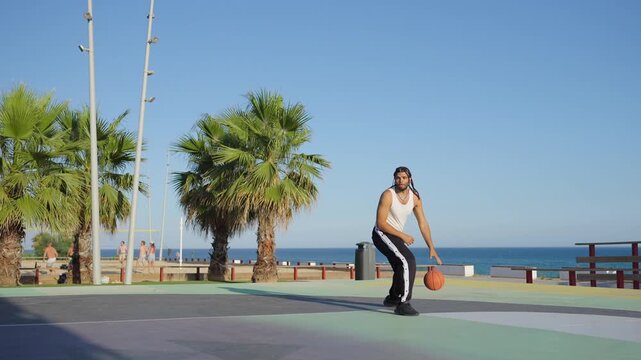Athletic man playing basketball on outdoor seaside court
