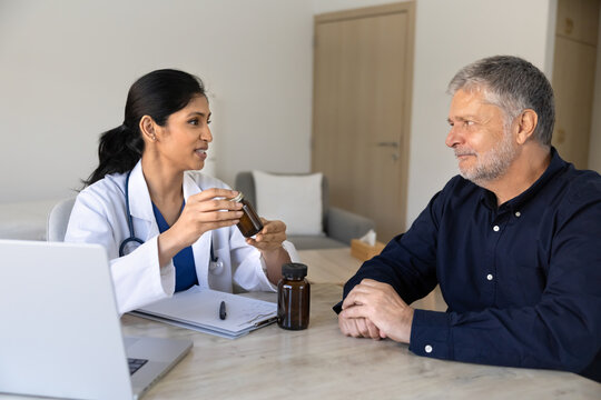 Woman doctor consulting senior man patient, discussing medicine bottle, sharing recommendation, explaining pills dosage during health checkup at hospital. Professional healthcare service, pharmacology