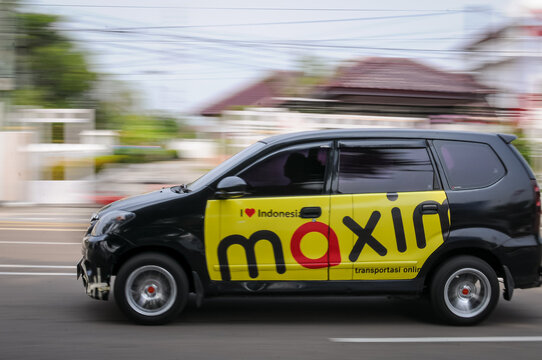 Riau-Indonesia, august 25th 2026 : a black passenger car featuring official yellow and red side branding for the ride-hailing and delivery service Maxim