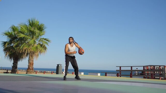 Athletic man playing basketball on a seaside court