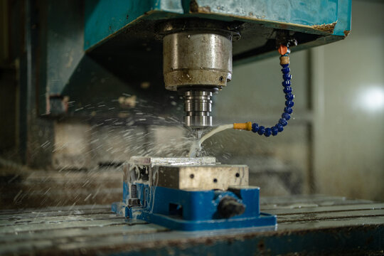 Industrial machinery detail in a vintage family metal workshop, sharp detail of the end mill cutting the aluminum block in the blue vise, heritage machinery of a family run factory