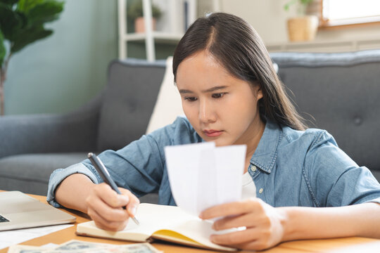 Debt asian young woman calculating money balance of finance from bill receipt and income on notebook, cost budget expenses for pay money form personal individual on table at home. Financial concept.