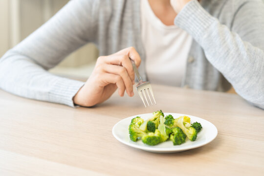 Diet in bored concept, Ketogenic, Low carb, Intermittent Fasting young woman dieting holding fork at broccoli on salad plate tired with eat fresh vegetables. Nutrition clean, healthy food good taste.