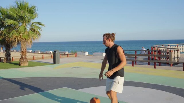 Young man dribbling and shooting basketball on seaside court