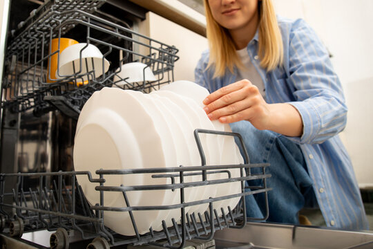Dishwasher. Woman unloads clean plates from dishwasher in functional kitchen