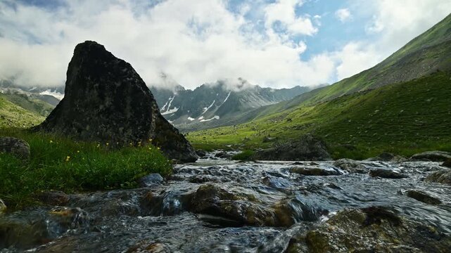 Mountain stream flowing through alpine valley with snow-capped peaks