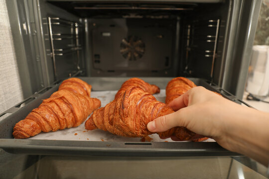 Croissants are being removed from oven, showcasing perfect golden brown color