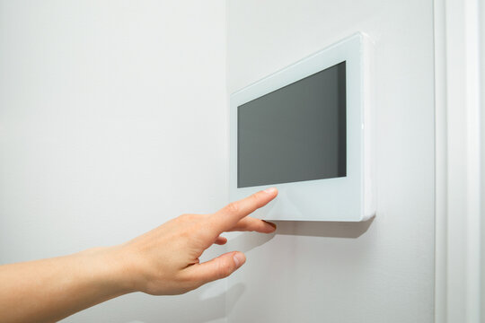 Hand interacts with touchscreen control panel mounted on wall