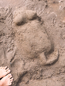 Mouse-shaped sand sculpture on beach beside bare feet, creative summer activity.
