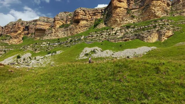 Person walking on grassy mountain slope below large cliffs
