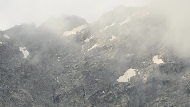 Dense clouds rolling over rocky mountain slope in timelapse