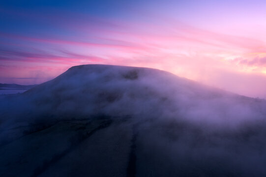 Aerial view of a mountain shrouded in thick morning mist under a vibrant pink and purple sky at sunrise in Sligo, County Sligo, Ireland.