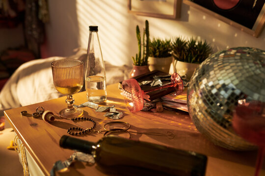 Messy wooden table after party with empty wine bottles, glasses, jewelry, and disco ball. Image suitable for youth lifestyle blogs, hangover recovery ads, or party cleanup services