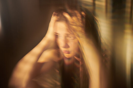 Caucasian teenager girl holding head in hands with blurry motion effect representing anxiety. Visual metaphor for mental health campaigns and youth psychological support