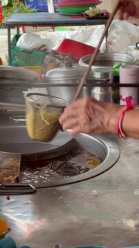 Street food cook preparing egg noodles in boiling water strainer in Bangkok Thailand