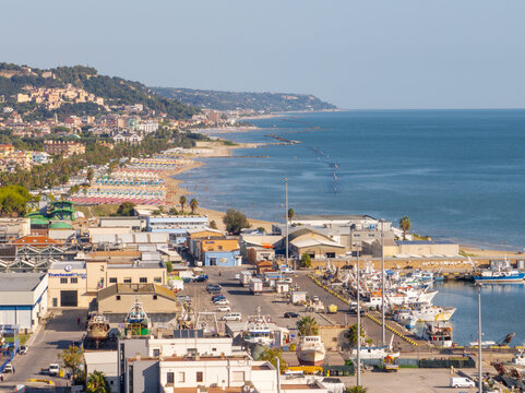 Aerial view of the harbor and sandy beach with fishing boats, rows of colorful umbrellas, and urban buildings in San Benedetto del Tronto, Marche, Italy.