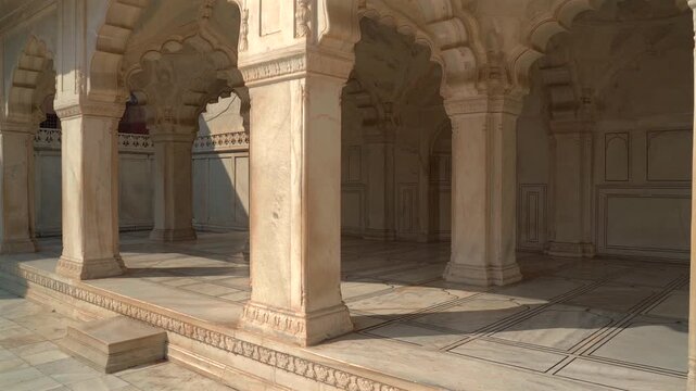 Wide shot of white marble pillars, cusped arches, and inlaid stone floor of a royal pavilion at Agra Fort in Uttar Pradesh, India.