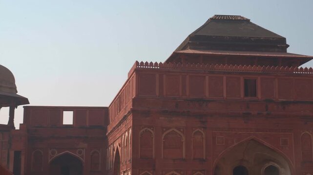 Horizontal pan right shot of a red sandstone chhatri pavilion and the facade of Jahangiri Mahal at Agra Fort in Uttar Pradesh, India.