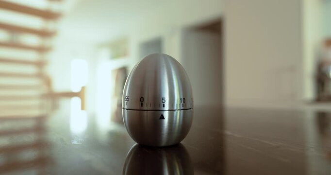 Close-up of a hand setting a metal egg timer on a kitchen counter, representing countdown, cooking time, deadlines, waiting, and time management.