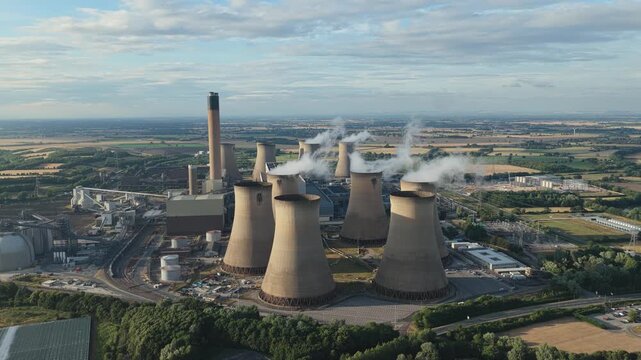 Aerial view of the large Drax Power Station in North Yorkshire with white steam rising from the cooling towers into the bright blue sky during a calm afternoon surrounded by green fields