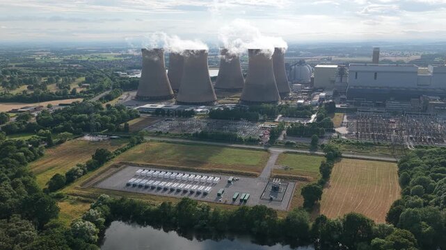 Aerial view of the large Drax Power Station with white smoke rising from cooling towers near fields and a lake under a bright daytime sky showing energy production in North Yorkshire England