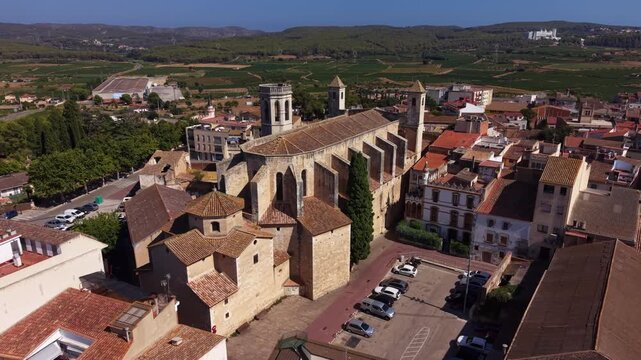 Sant Julia de l'Arboc town center in Catalonia, Spain, featuring a medieval stone church surrounded by terracotta-roofed buildings, vineyards and green hills in background