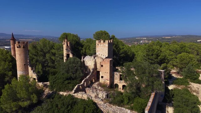 Ruins of Castell de la Muga rising above pine forest in Catalonia, Spain, with medieval stone towers, battlements and crumbling walls under a clear blue sky