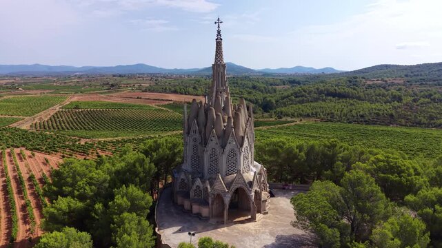 Santuari de la Mare de Deu de Montserrat sanctuary rises above vineyards and forested hills in Catalonia, Spain, its gothic spires reaching toward a clear blue sky
