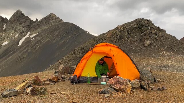 Male camper melting snow medium view inside a tent with a gas stove in Svaneti, Georgia, showing expedition water preparation, camp cooking, high-altitude survival, and backpacking logistics.
