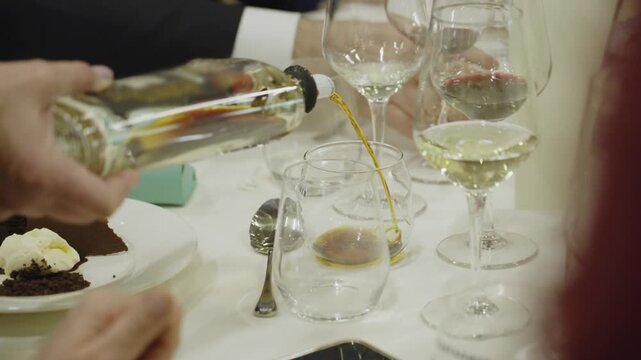 Waitstaff pours brown liqueur into glass at formal banquet dinner table setting.