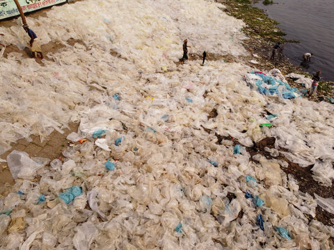 Aerial view of massive amounts of discarded plastic bags polluting the banks of the Buriganga River with people working nearby in Dhaka, Bangladesh.