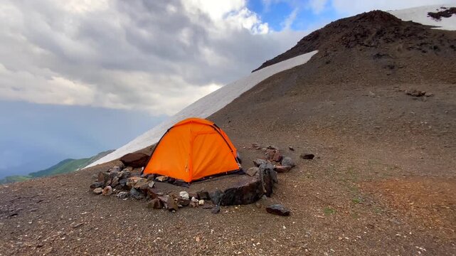 Orange tent sheltering hikers wide view at 3300 meters opposite Mount Ushba in Svaneti, Georgia, showing high-altitude camping, alpine bivouac logistics, weather exposure, and mountain trekking.