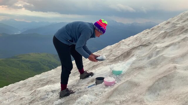 Hiker collecting clean snow in side view on alpine slope in Svaneti, Georgia, outdoor scene for gas stove melting, water preparation, expedition logistics, backcountry camping, and trekking survival.