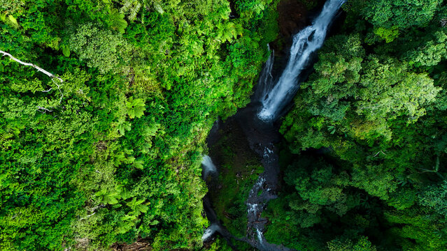 Aerial view of Curug Ciarjuna waterfall cascading through dense tropical rainforest with lush green foliage and rocky terrain Garut, West Java, Indonesia.
