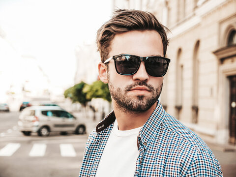 Portrait of handsome confident stylish hipster lambersexual model.Man dressed in white T-shirt. Fashion male posing on the street background in sunglasses