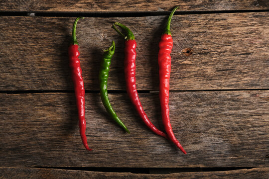 Three red and one green chili peppers lined up on wooden plank.