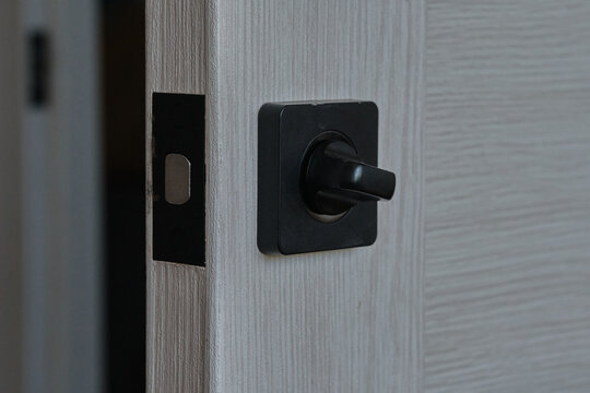 Black square door rotary lock latch fitted on edge light wood interior door.
