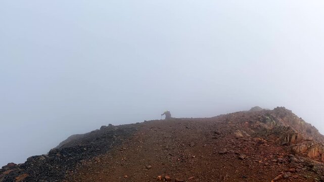 Hiker trekking wide view along a foggy rocky ridge in Svaneti, Georgia, showing low-visibility route conditions, high-altitude navigation, endurance hiking, and mountain travel risk assessment. 