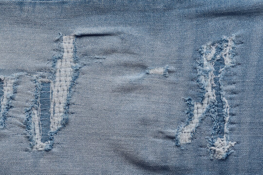 Overview light blue denim fabric with multiple ripped areas and exposed white threads.