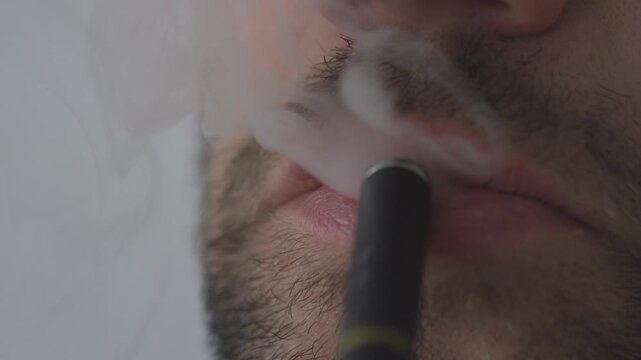 Extreme close up of man lips exhaling thick white vapor from electronic cigarette device in slow motion.