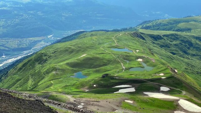 Koruldi Lakes spreading in elevated wide view across green ridges above Mestia, Georgia, for mountain tourism, travel promotion, hiking destination marketing, and alpine landscape editorial use