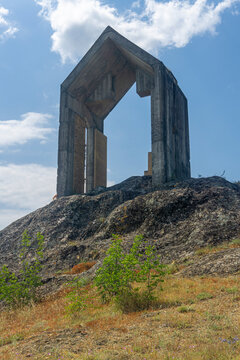 A roofed stele on the top of a rocky hill dedicated to the builders of the Algeti Reservoir. A blue sky with clouds in the background.