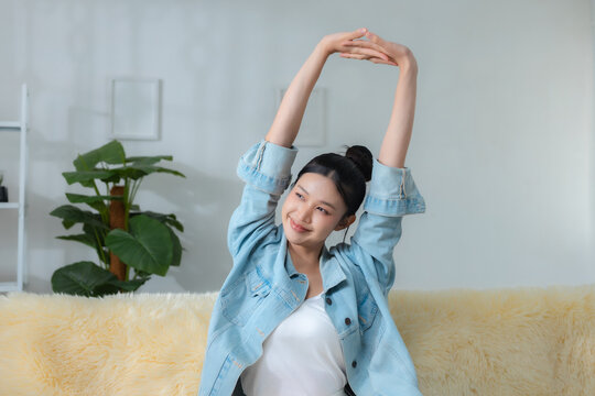 smiling woman stretching her arms while relaxing on sofa at home, enjoying calm morning and healthy lifestyle, wellness, stretching, relaxation, health.