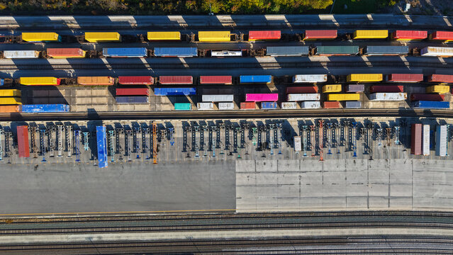 Aerial view of a busy rail yard filled with colorful shipping containers on flatbed rail cars and parallel tracks in Columbus, Ohio, United States.