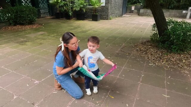 A young Latina mother and her 2-year-old son are seen outdoors, intently reading a map together. They are planning their route and discussing their visit before entering the zoo, showing family bondin